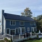 Solar panels installed on a two-story colonial home in Connecticut with blue siding, white trim, and a backyard deck