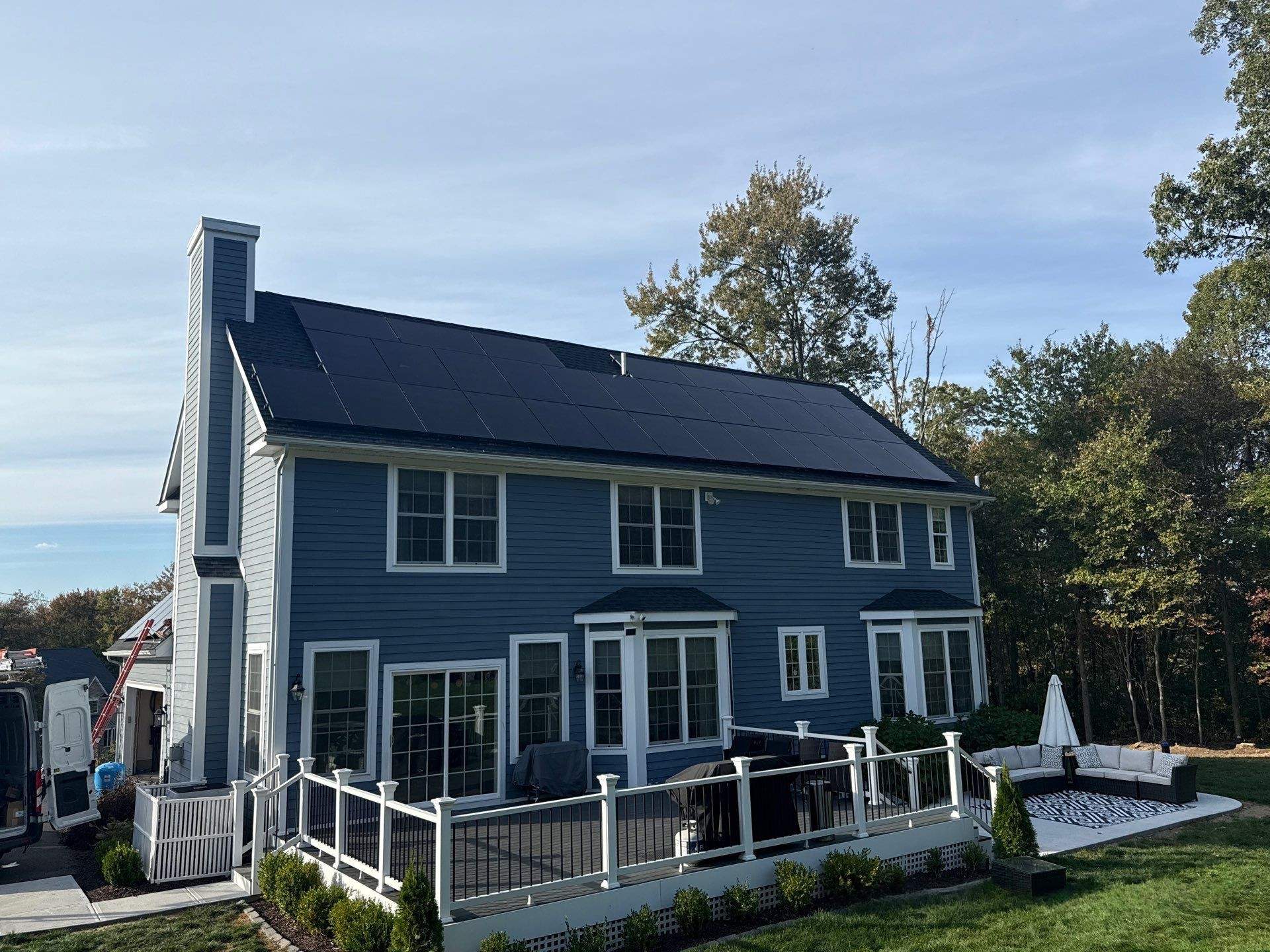 Solar panels installed on a two-story colonial home in Connecticut with blue siding, white trim, and a backyard deck